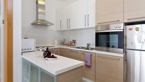 Una cucina moderna con mobili bianchi, elettrodomestici in acciaio inossidabile e un'isola centrale con un asciugamano viola.