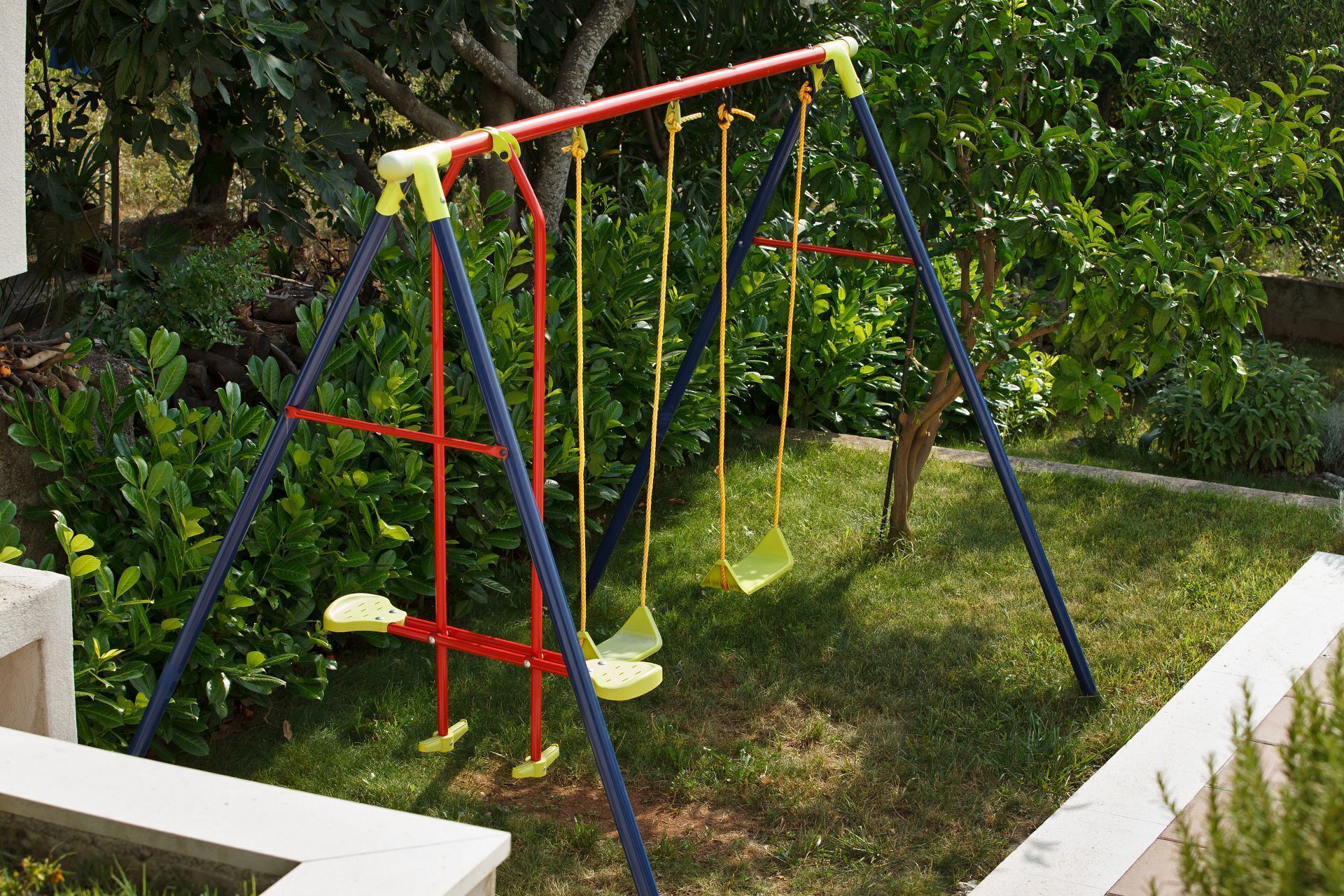 Un columpio en un jardín con un sendero de concreto y follaje verde.