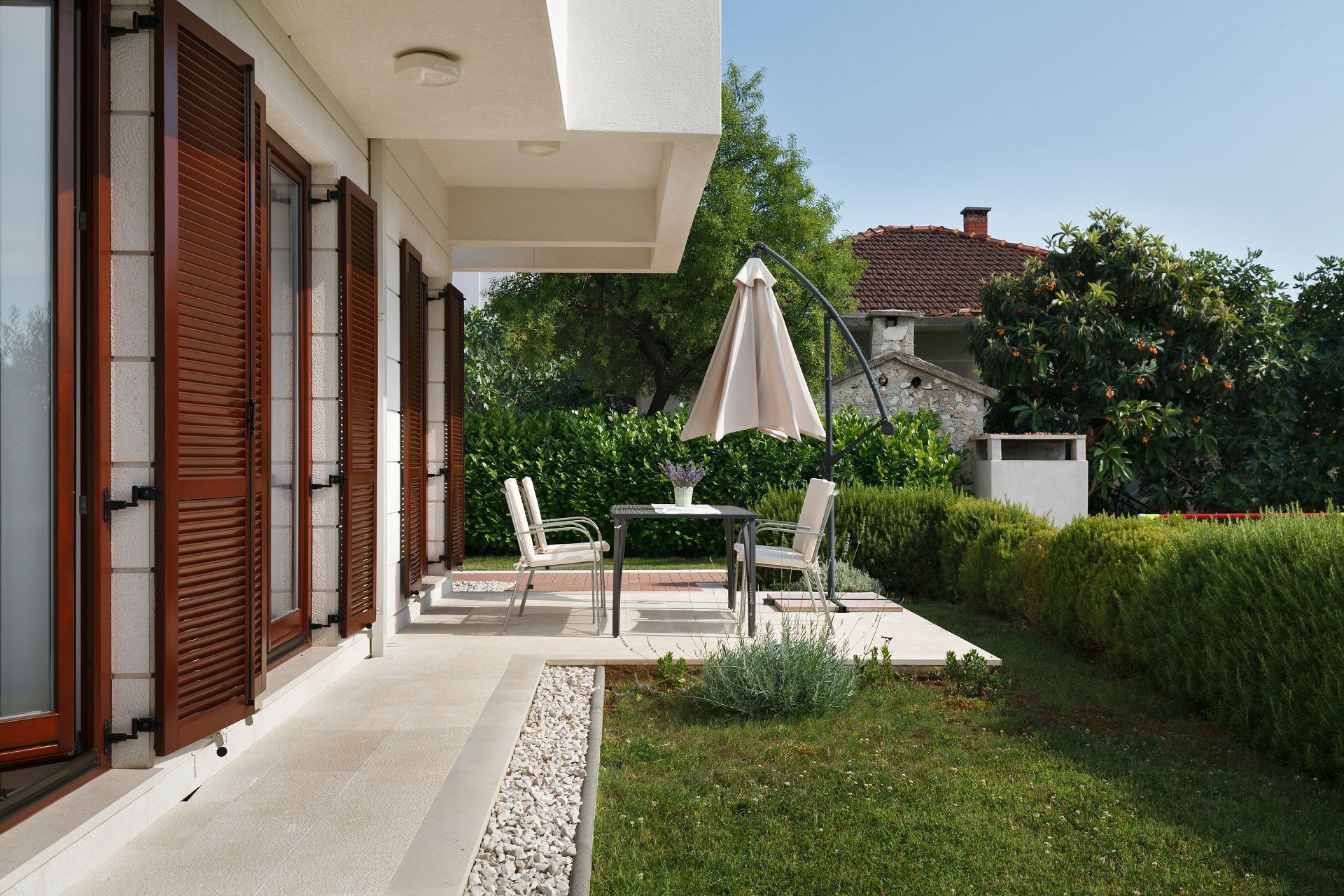 A patio with a table and chairs, a beige umbrella, and a stone wall in the background.