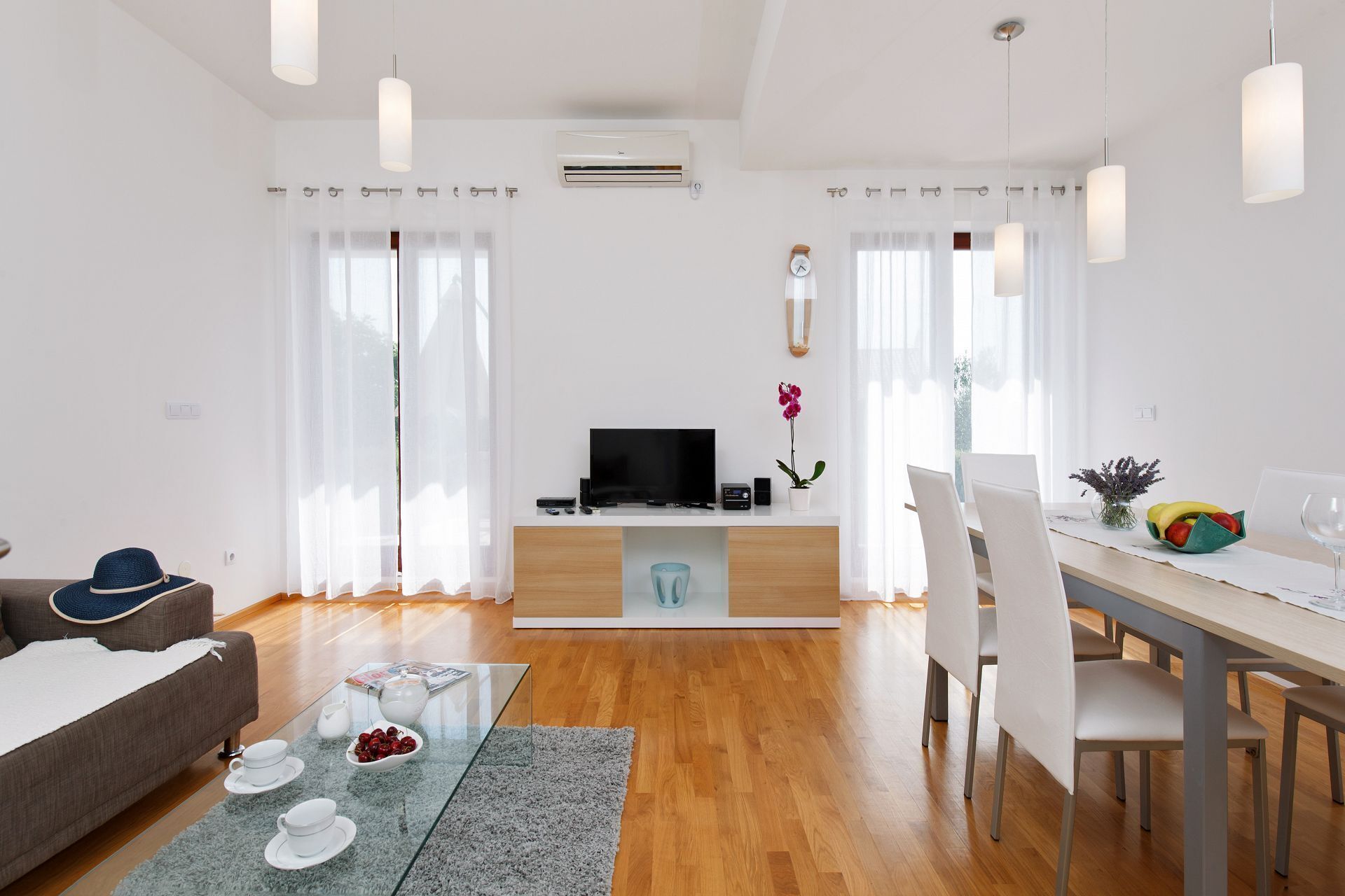A modern living room with a flat-screen TV, a dining area with a table and chairs, and a sofa.