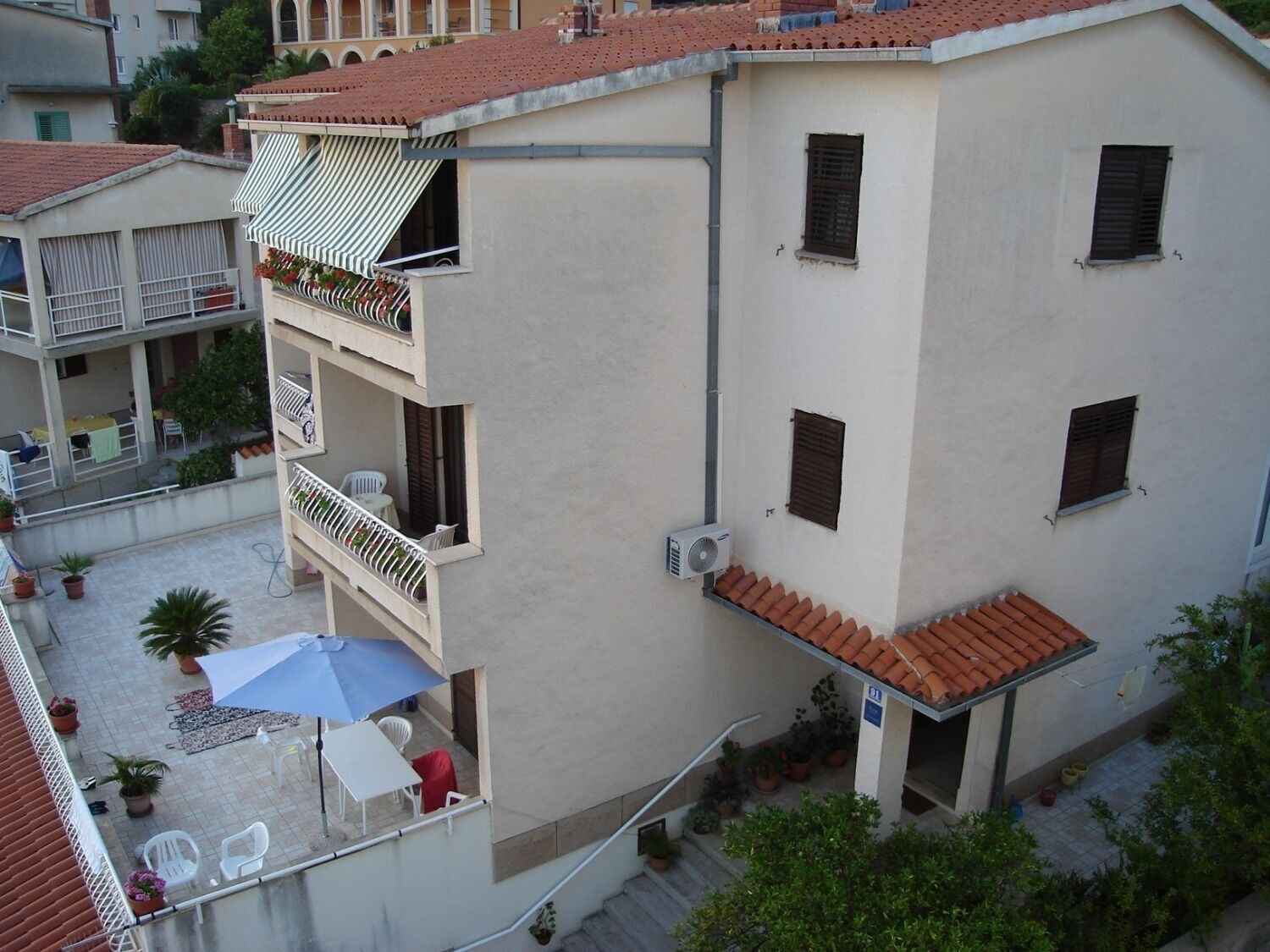 A multi-story building with balconies, outdoor seating, and potted plants.
