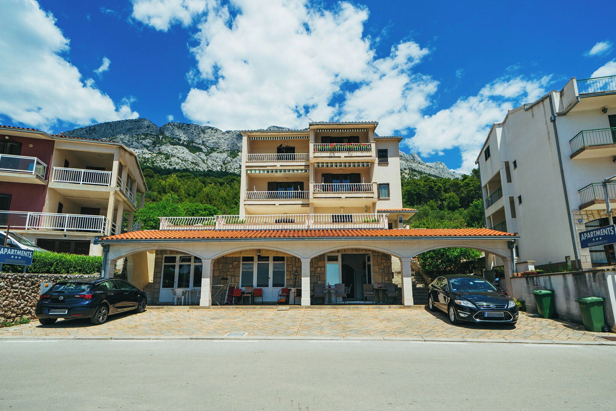 A multi-story building with a covered entrance, balconies, and a mountainous backdrop.