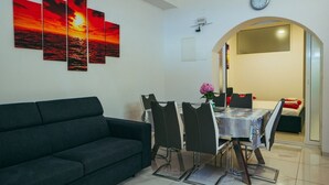 En moderne stue med en mørk sofa, et spisebord med stole og et vægmonteret ur.