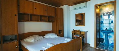 A wooden-framed bed with a nightstand, a desk with a chair, and a bathroom with a sink and mirror.