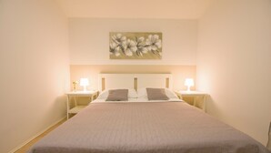 Ein ordentlich bezogenes Bett mit einer gesteppten Decke, zwei Nachttischlampen und einem floralen Gemälde an der Wand.
