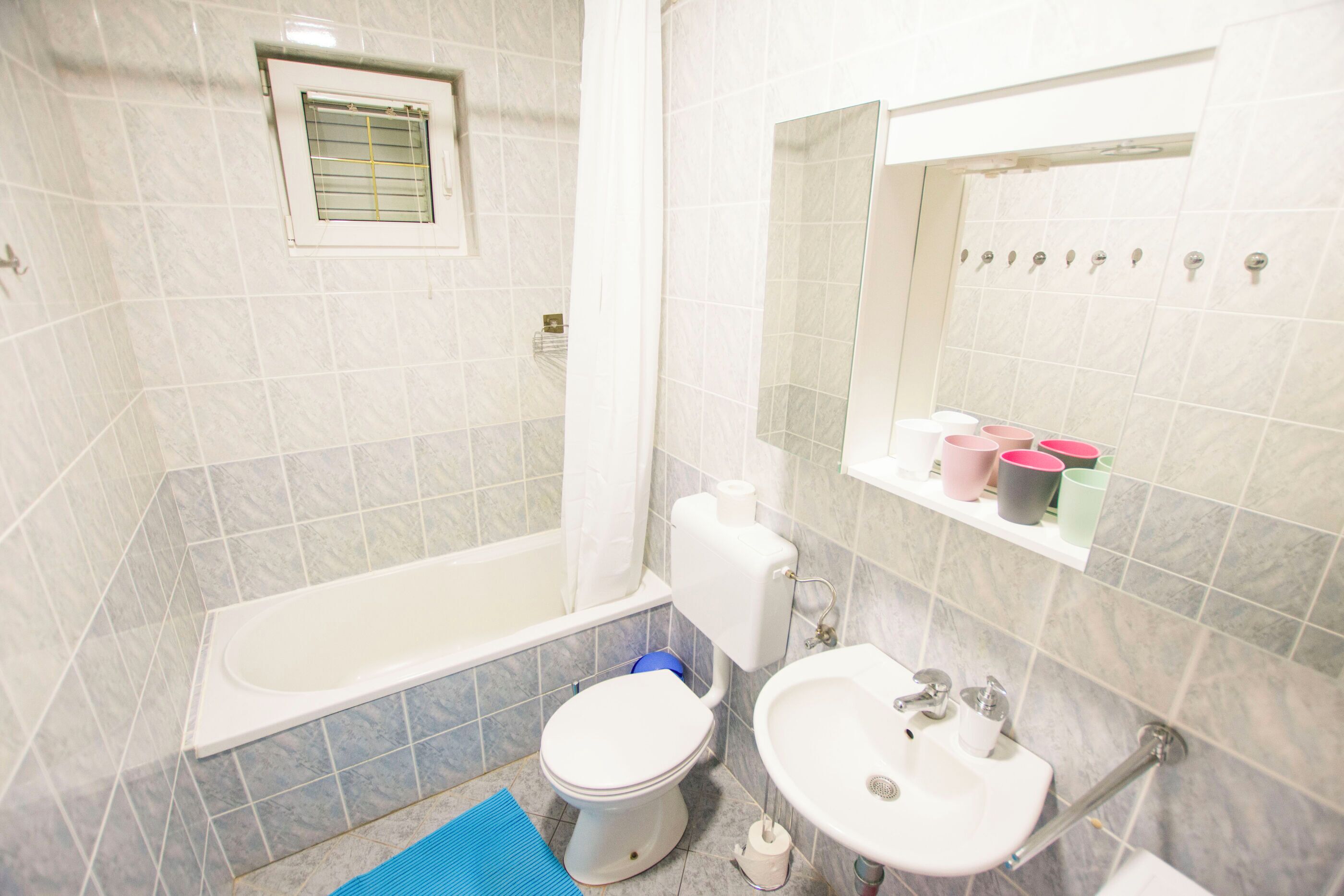 Une salle de bain équipée d’une baignoire, de toilettes, d’un lavabo et d’une fenêtre avec un rideau.