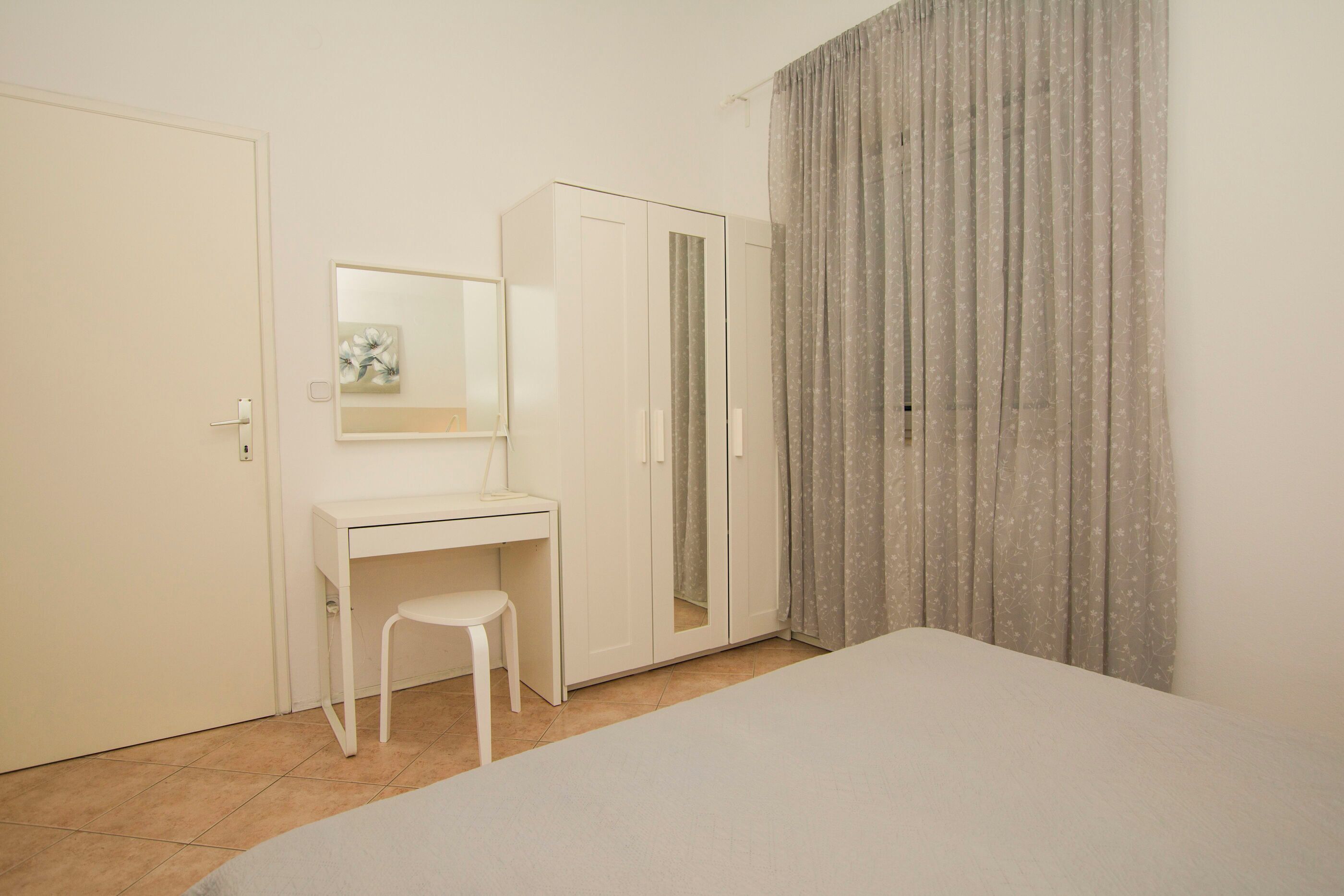Ein Schlafzimmer mit Bett, Schreibtisch, Stuhl, Kleiderschrank und Spiegel.