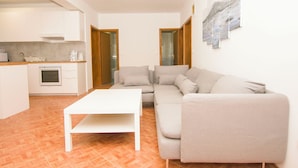 Ein modernes Wohnzimmer mit einem weißen Sofa, einem weißen Couchtisch und einer Küchenzeile mit weißen Schränken und einer Arbeitsplatte.