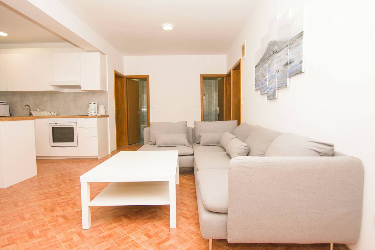 A modern living room with a white sofa, a white coffee table, and a kitchen area with white cabinets and a countertop.