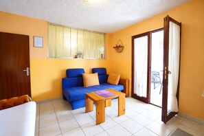 A living room with a blue sofa, a wooden coffee table, and a sliding glass door leading to an outdoor area. - Apartment Lile (Omis)