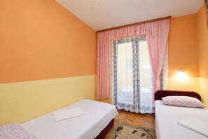 A room with two beds, a window with lace curtains, and a wall-mounted light. - Apartment Lile (Omis)
