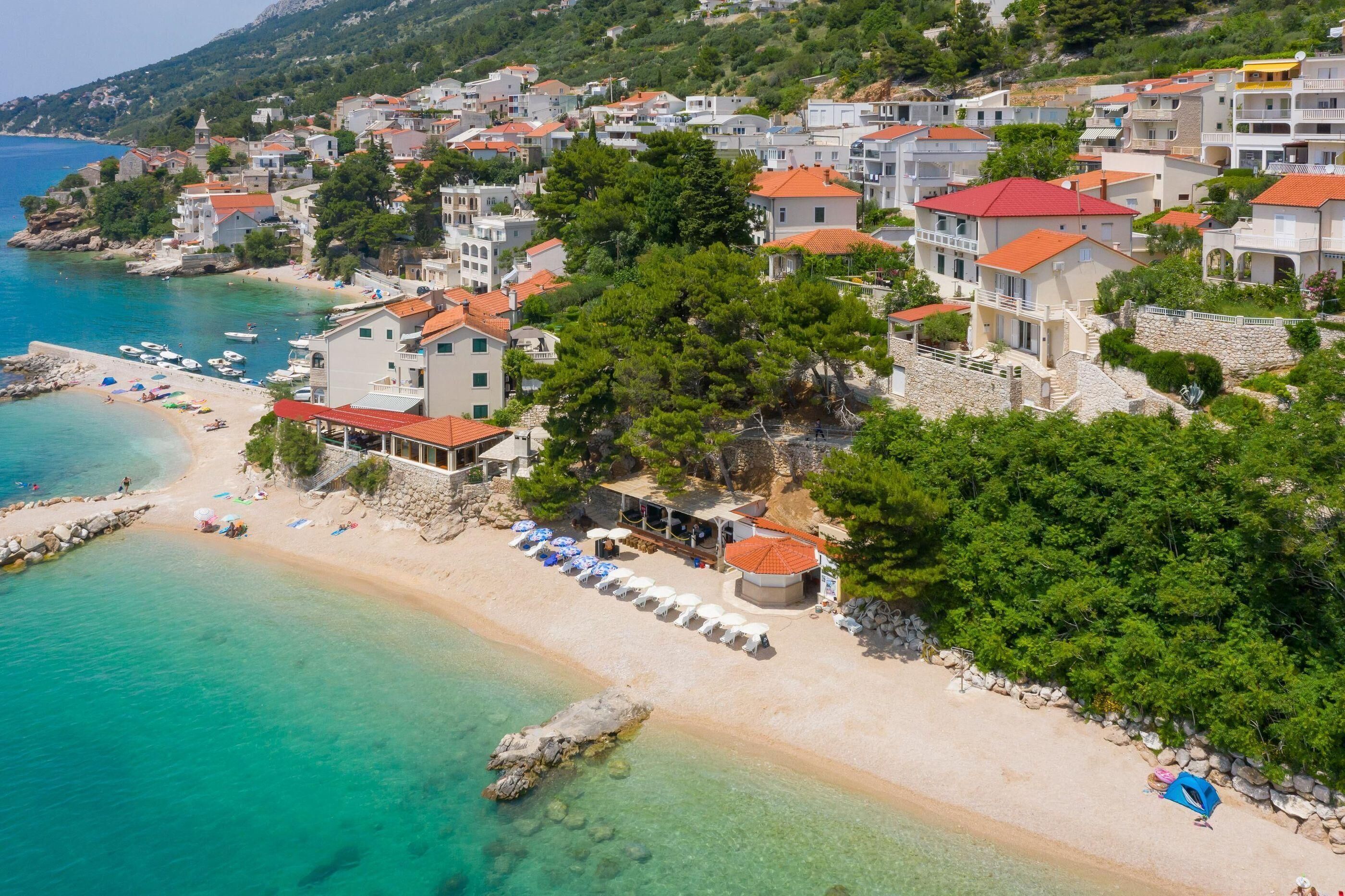 Uma vila costeira com praia, águas claras e edifícios com telhados vermelhos.