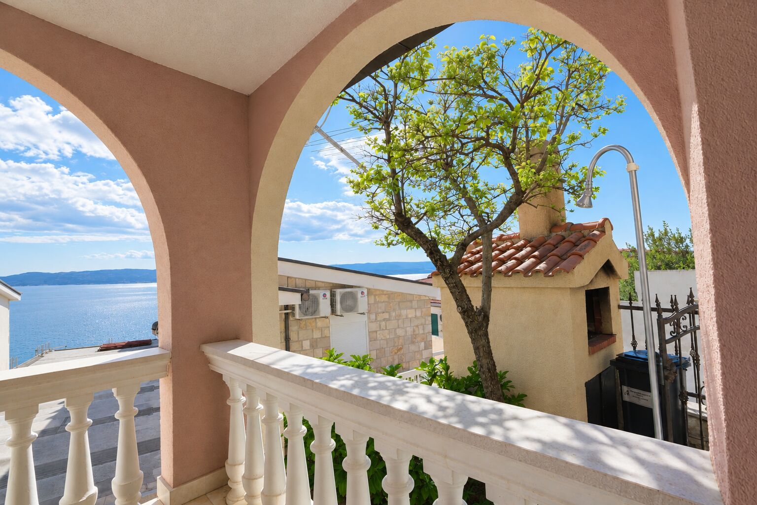 A balcony with a view of the sea and a tree.