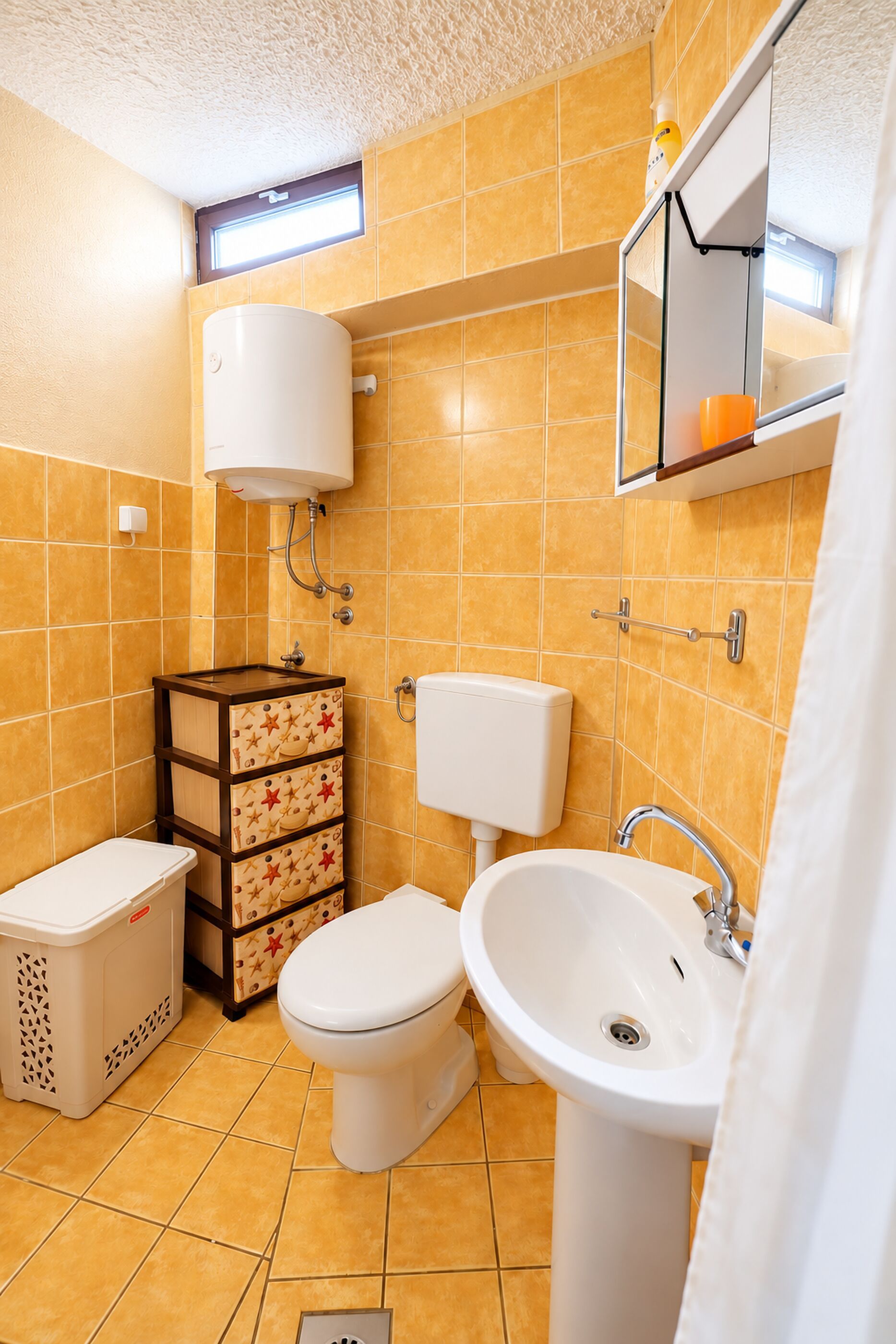 A bathroom with a toilet, sink, and storage unit.