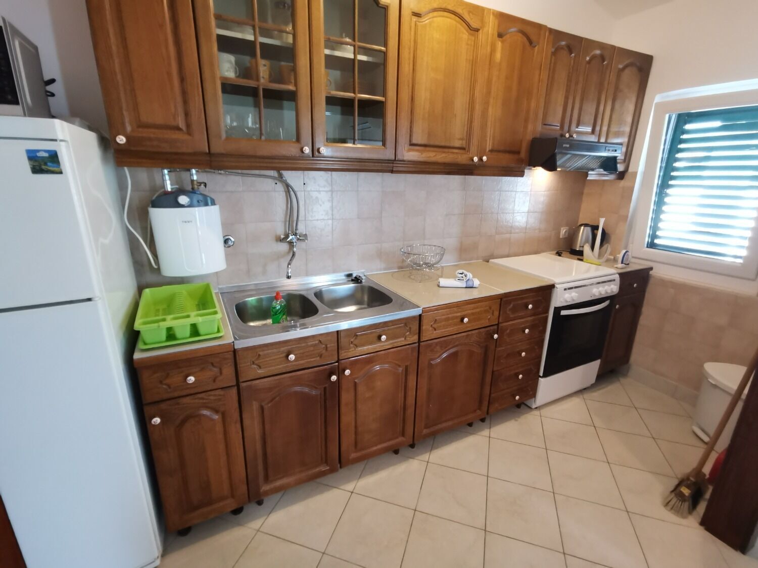 A kitchen with wooden cabinets, a sink, a dishwasher, and a window with blinds.