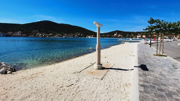 Ein Küstenweg mit freiem Blick auf das Meer und einem entfernten Berg.