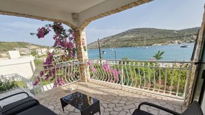 Ein Balkon mit zwei schwarzen Korbstühlen, einem kleinen Tisch und Blick auf das Meer mit Booten.