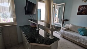 Eine moderne Küche mit Marmorarbeitsplatte, einem darüber montierten Fernseher und einer Glastür, die auf einen Balkon führt.