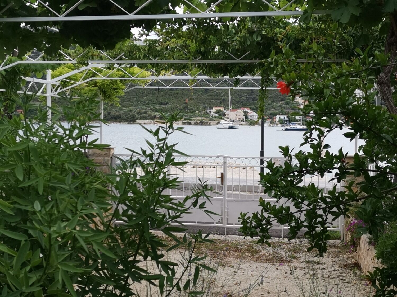 A view of a coastal area with a metal fence, greenery, and a body of water with boats.