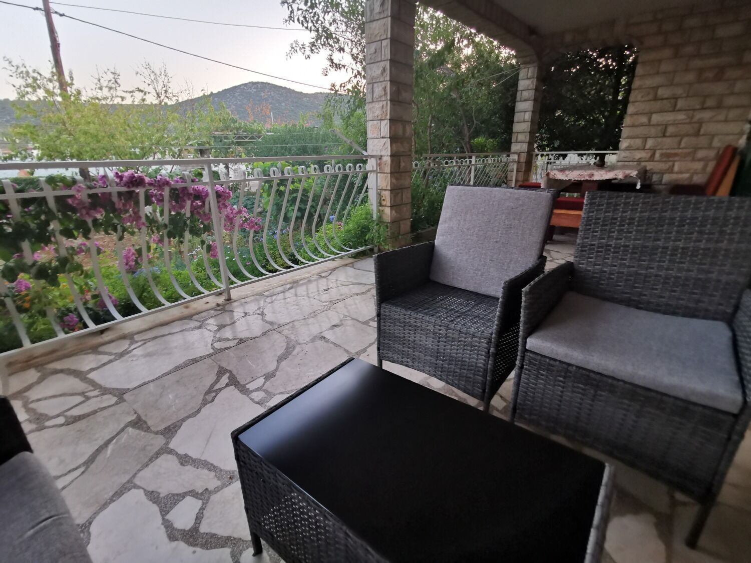 A covered outdoor seating area with wicker furniture and a stone floor.