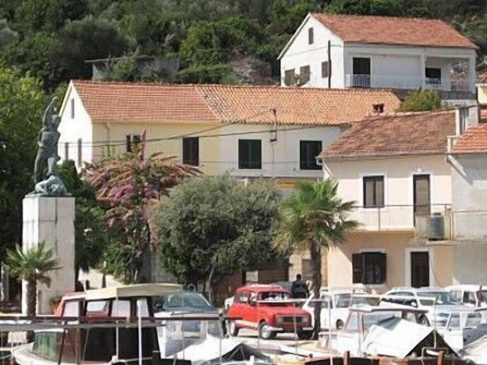 A coastal building with a tiled roof, surrounded by parked cars and a statue.