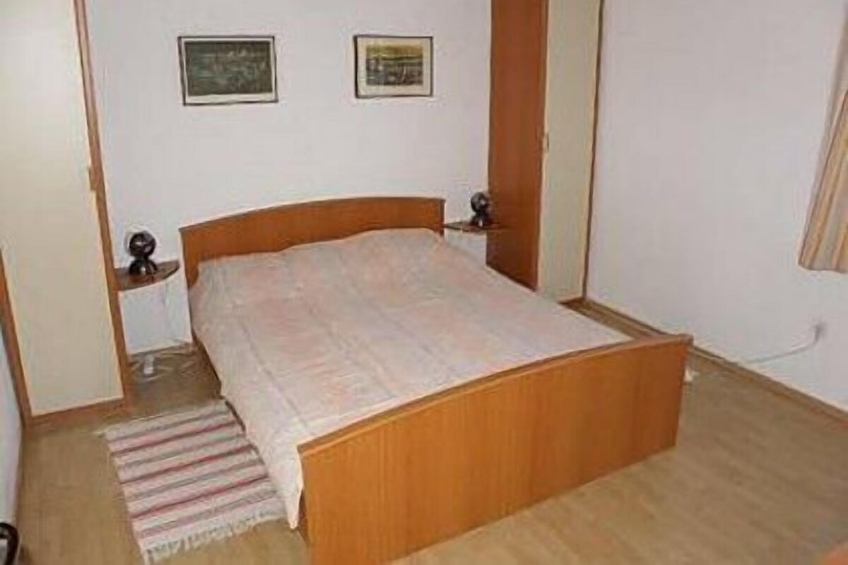 Ein Schlafzimmer mit einem hölzernen Bett, einem Nachttisch, zwei gerahmten Bildern an der Wand.