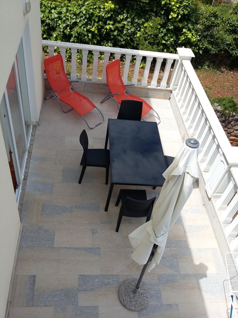 Une terrasse avec une table et des chaises, une balustrade blanche et de la verdure en arrière-plan.