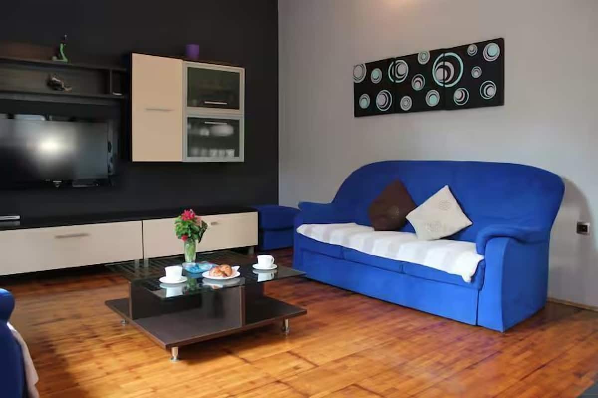 A modern living room with a blue sofa, a glass coffee table, and a flat-screen TV on a black cabinet.