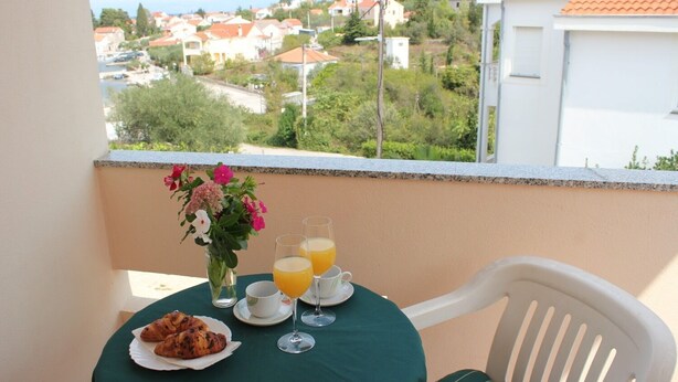 En balkong med ett bord dukat för frukost, med bland annat croissanter och apelsinjuice, med utsikt över ett bostadsområde.