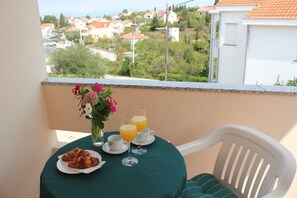 A balcony with a table set for breakfast, including croissants and orange juice, overlooking a residential area. - Apartments Ruzica (Preko)