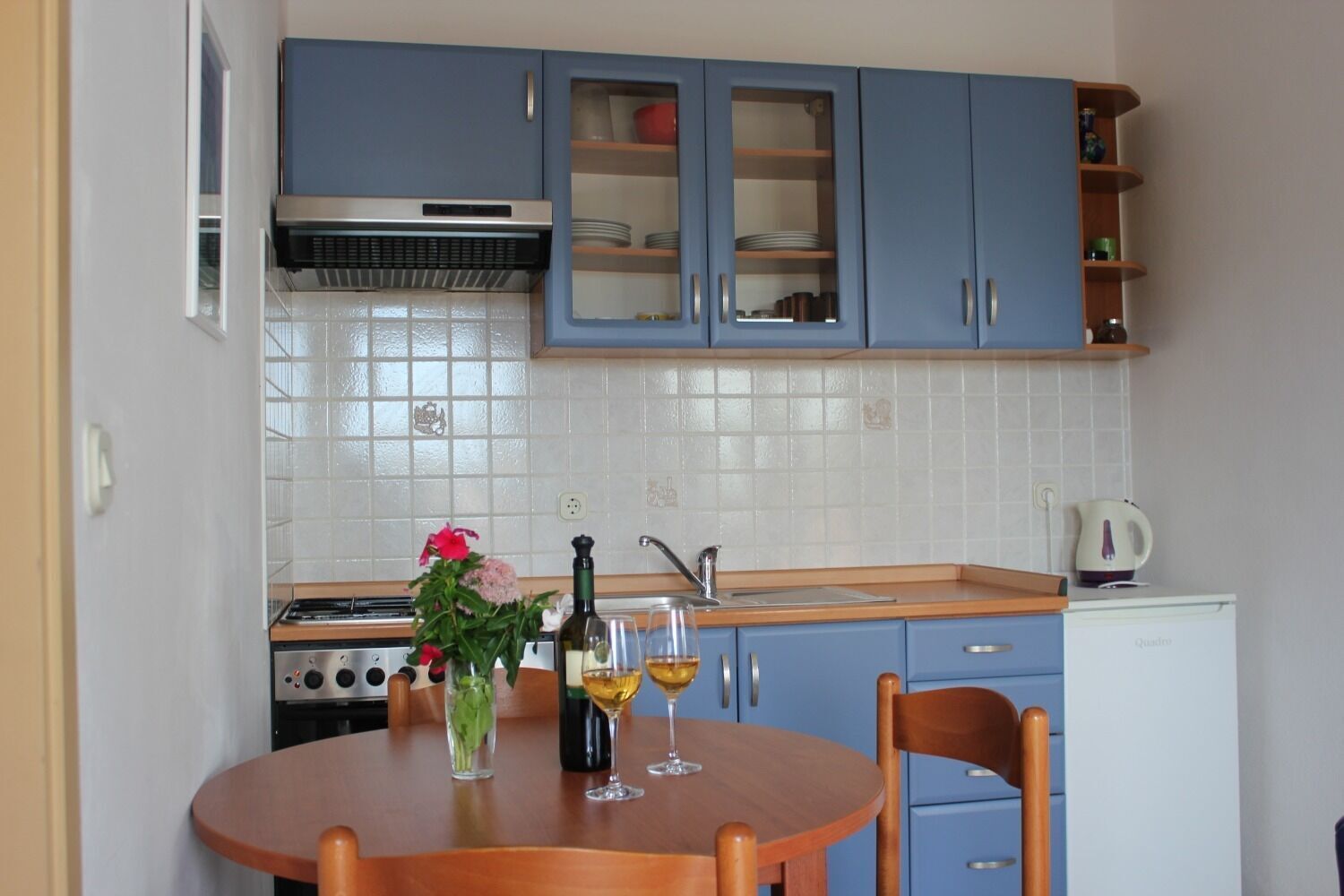 A compact kitchen with blue cabinets, a white tiled backsplash, a stove, and a small refrigerator.