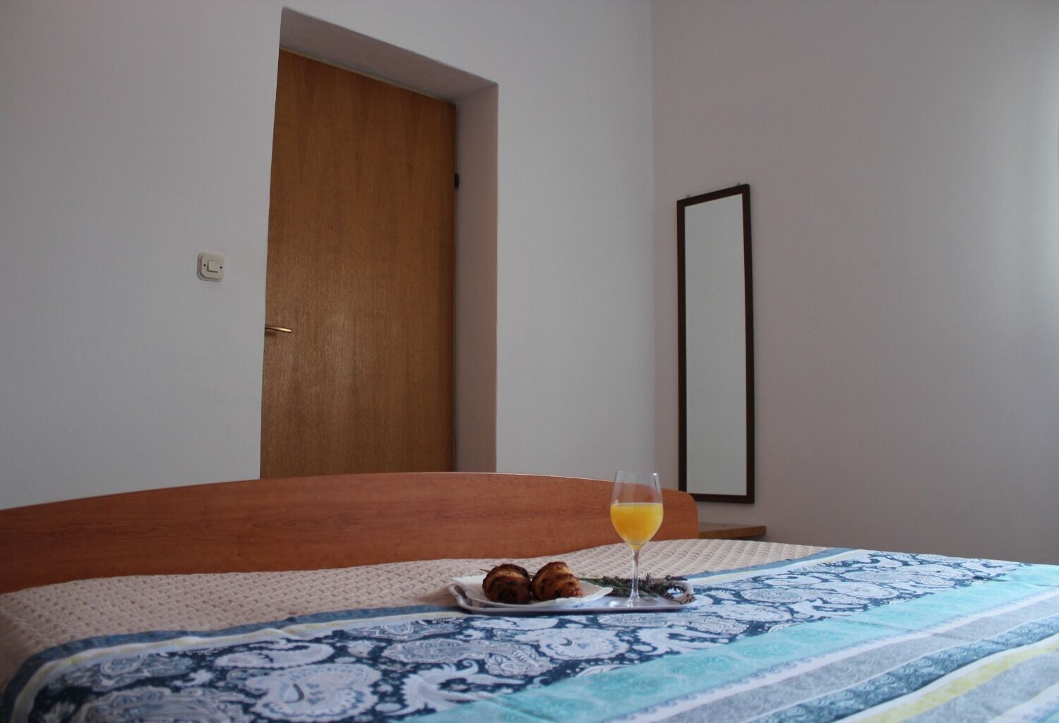 A bedroom with a bed, a bedside table with a glass of orange juice, and a plate with a croissant.
