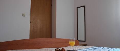 A bedroom with a bed, a bedside table with a glass of orange juice, and a plate with a croissant.