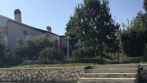 A stone staircase leading down to a clear water body, with a building and trees in the background. - Apartments Andy (Sukosan)