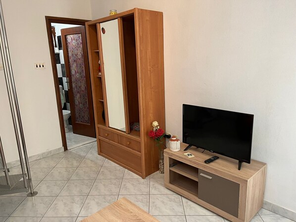 Une pièce avec une armoire en bois, un téléviseur posé sur un meuble en bois et un sol carrelé.