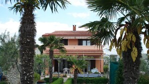 A two-story house with a tiled roof, surrounded by a garden with palm trees and a small pond. - Apartments Andy (Sukosan)