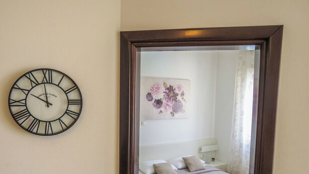 A bedroom with a bed, pillows, a bedside table, a nightstand, a wall clock, and a floral artwork. - Apartments Eddie (Zadar)