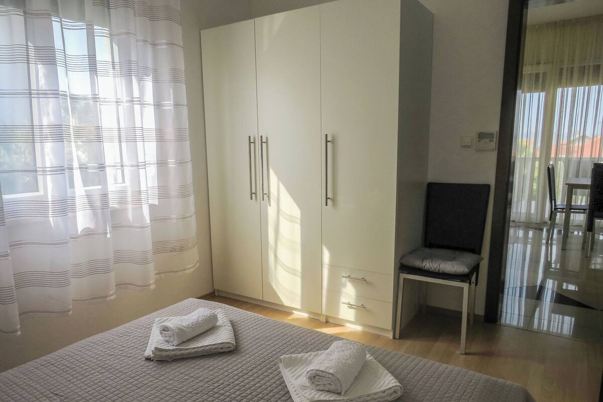 A bedroom with a bed, a wardrobe, a chair, and a window with curtains.
