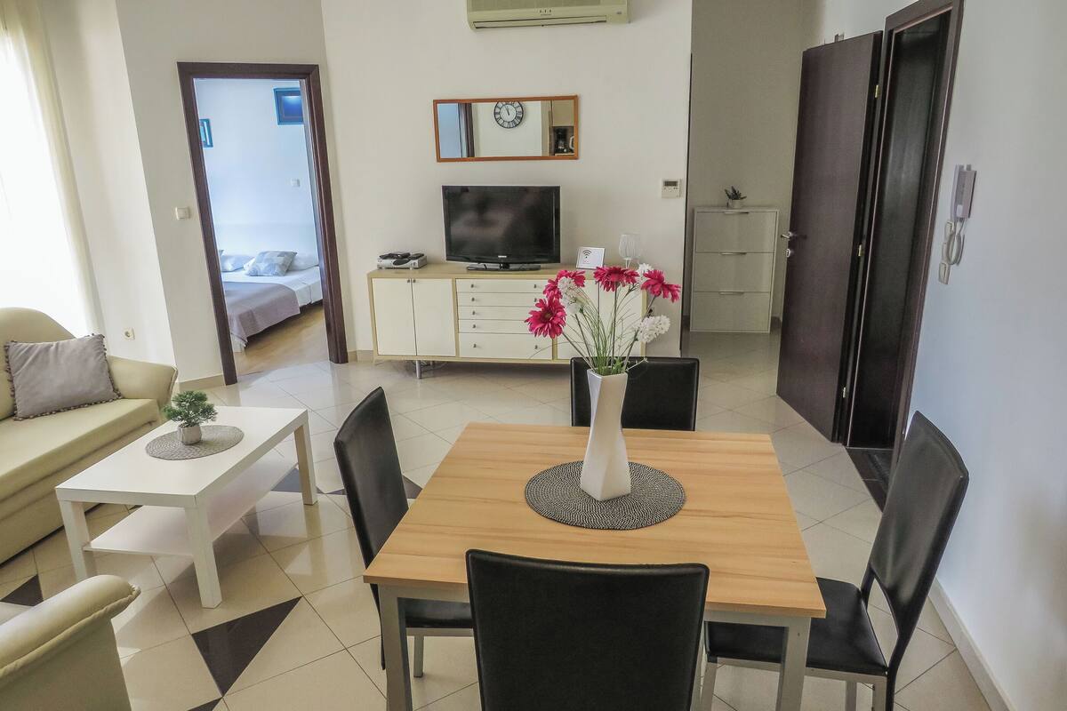 A dining area with a table, chairs, a vase of flowers, a TV, and a cabinet.