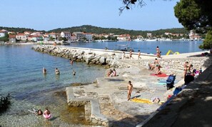 A coastal area with a rocky shoreline, clear water, and people engaging in water activities. - Apartment Ivy (Kukljica)