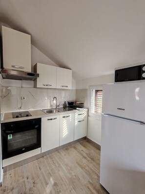A modern kitchen with white cabinets, a built-in oven, a microwave, and a refrigerator. - Apartment Ivy (Kukljica)