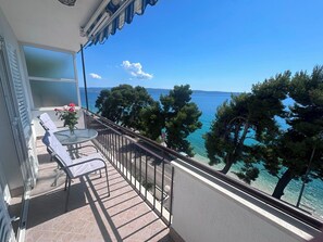 Een balkon met een tafel, stoelen en uitzicht op zee.