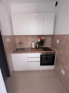 A kitchen with white cabinets, a sink, a stove, and a vase with flowers. - Apartment Verica (Dugi Rat)