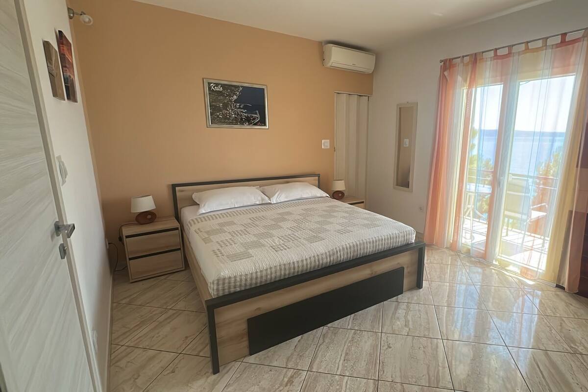 A bedroom with a bed, bedside tables, an air conditioner, a window with curtains, and a wall-mounted picture.