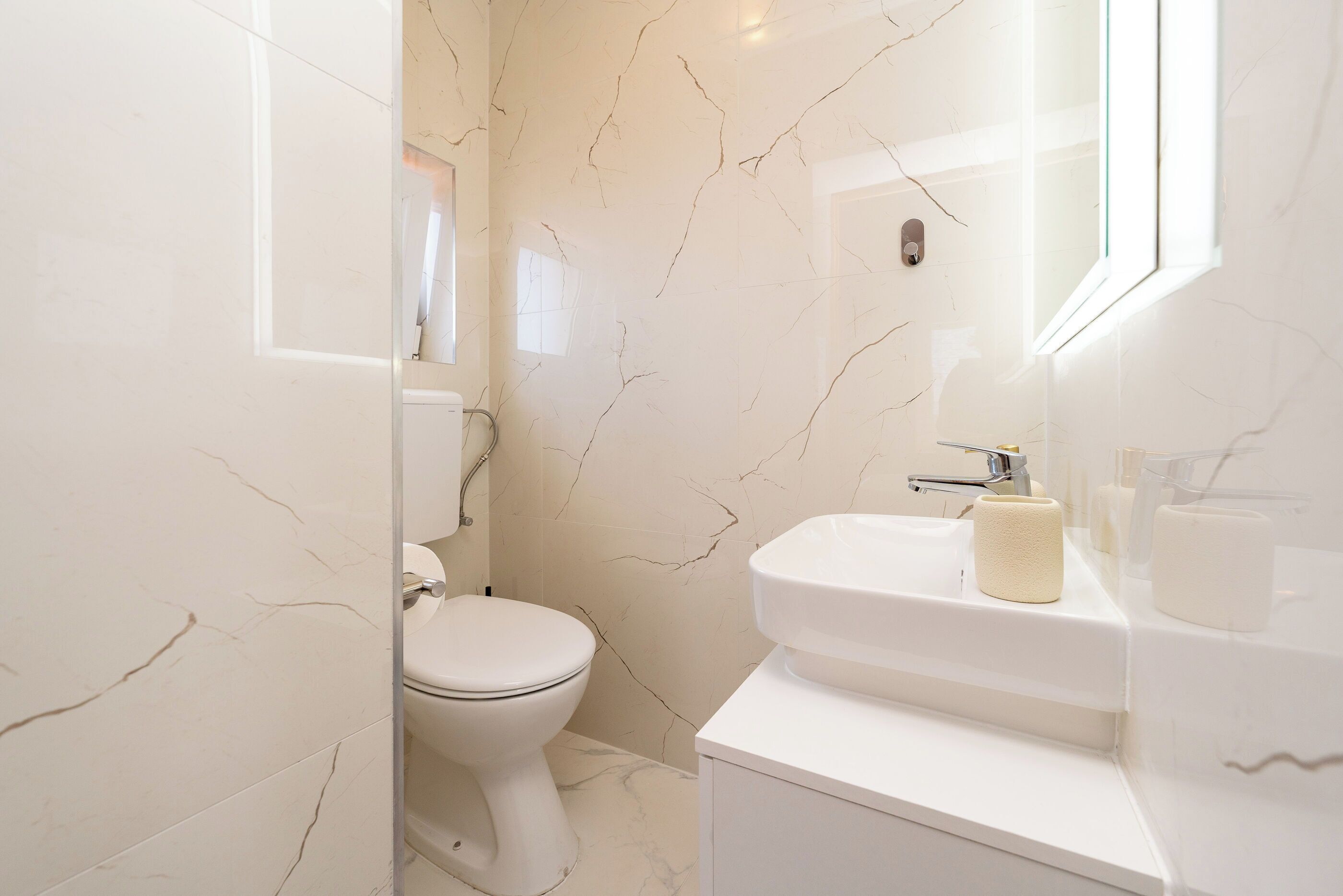 A bathroom with a toilet, sink, and marble walls.