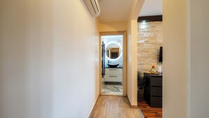 A hallway with a wooden floor, a kitchen area with a stone backsplash, and a modern light fixture.