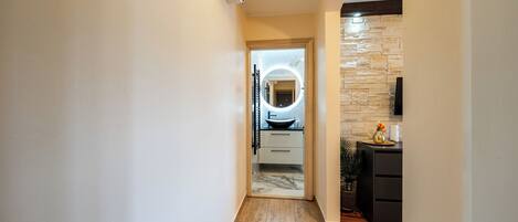 A hallway with a wooden floor, a kitchen area with a stone backsplash, and a modern light fixture.