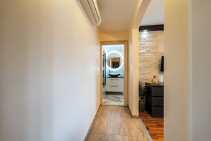 A hallway with a wooden floor, a kitchen area with a stone backsplash, and a modern light fixture. - Apartments Tomo (Sukosan)