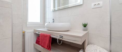 A modern bathroom with a white sink, a mirror, and a small potted plant.