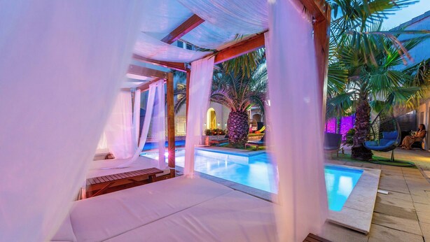 A poolside area with a covered seating area, a small pool, and palm trees.